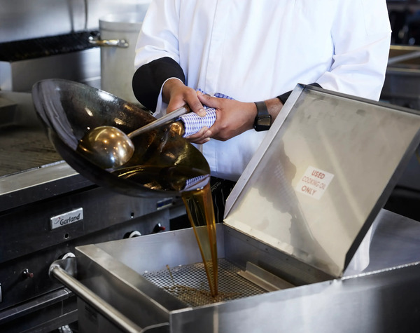 A cook pouring used frying oil from a wok into a fryer's collection tray